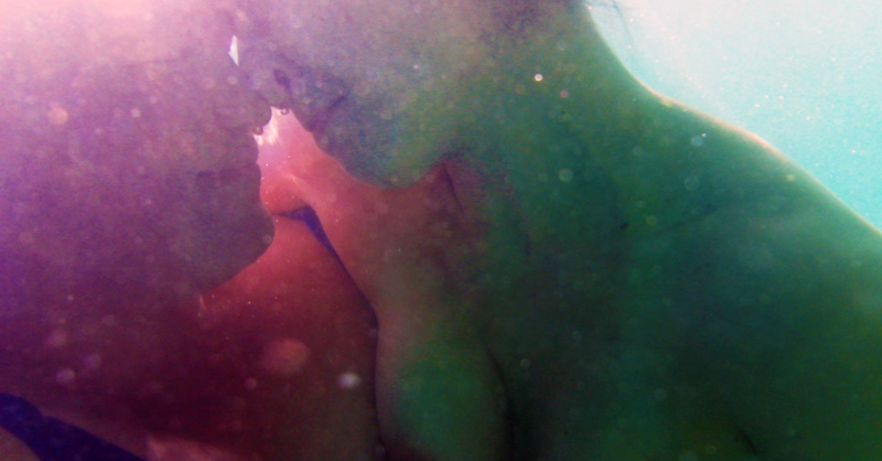 two women underwater in the ocean, pressing noses together in an intimate hongi, bubbles around them